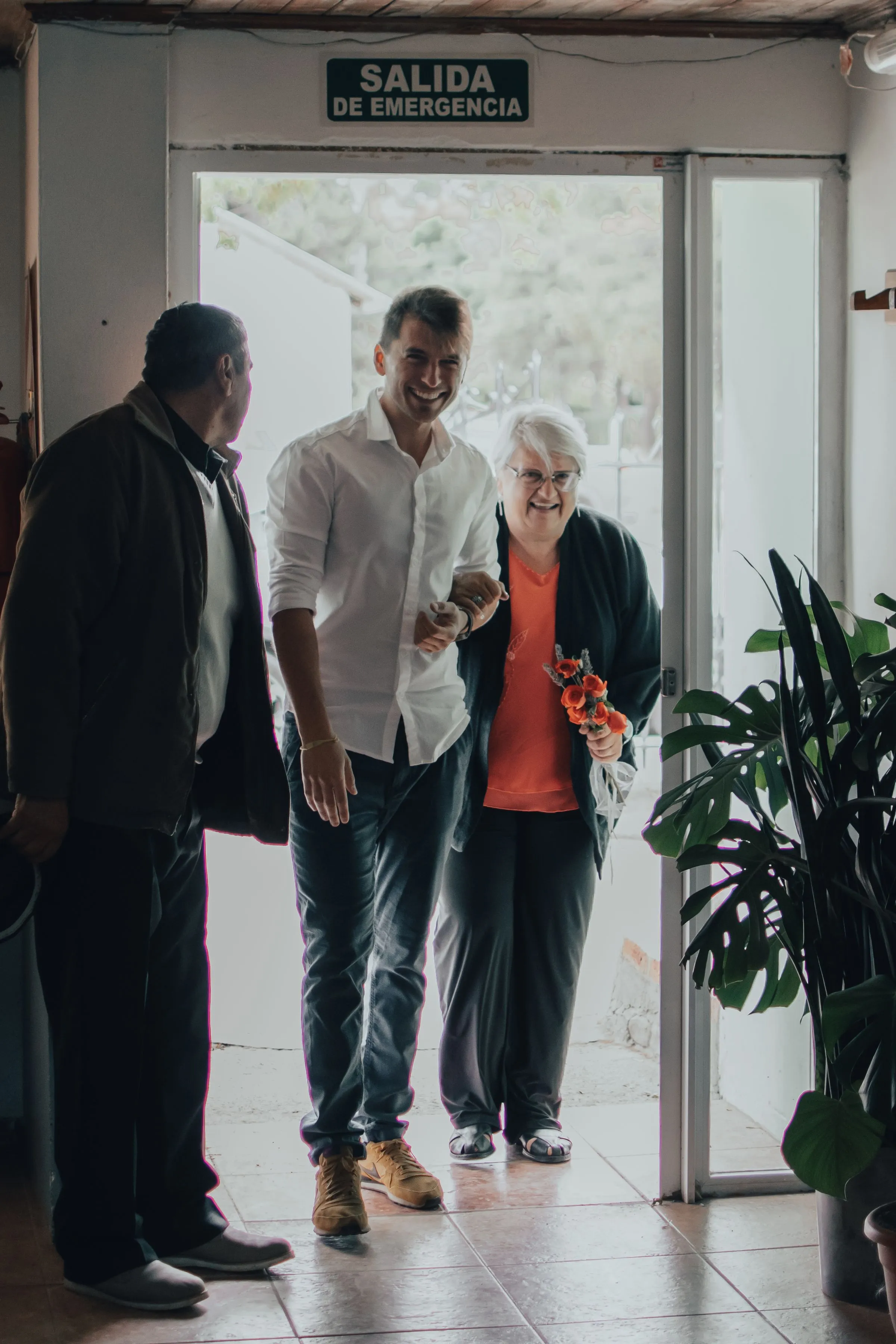 An older woman smiles as she walks out through glass doors with her family beside her