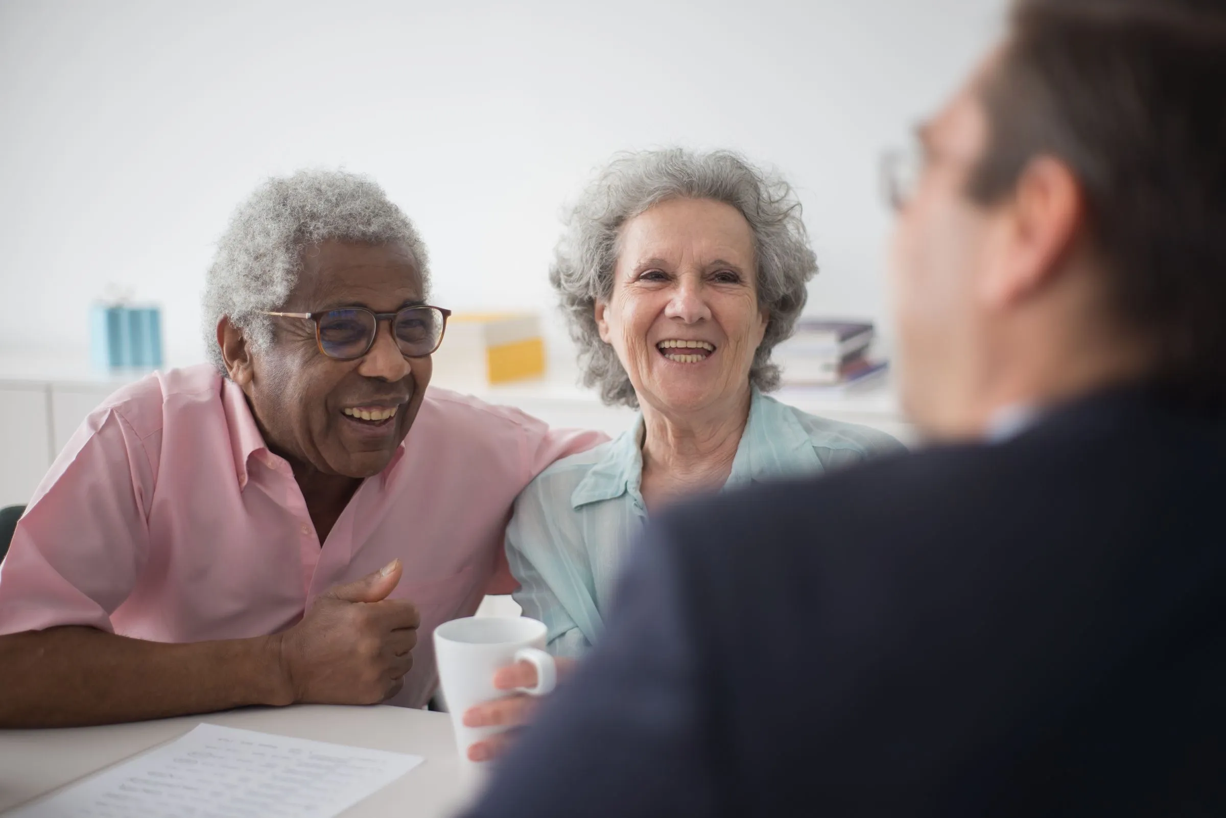 An older couple smile across a table at an advisor, coffee cups and papers in front of them