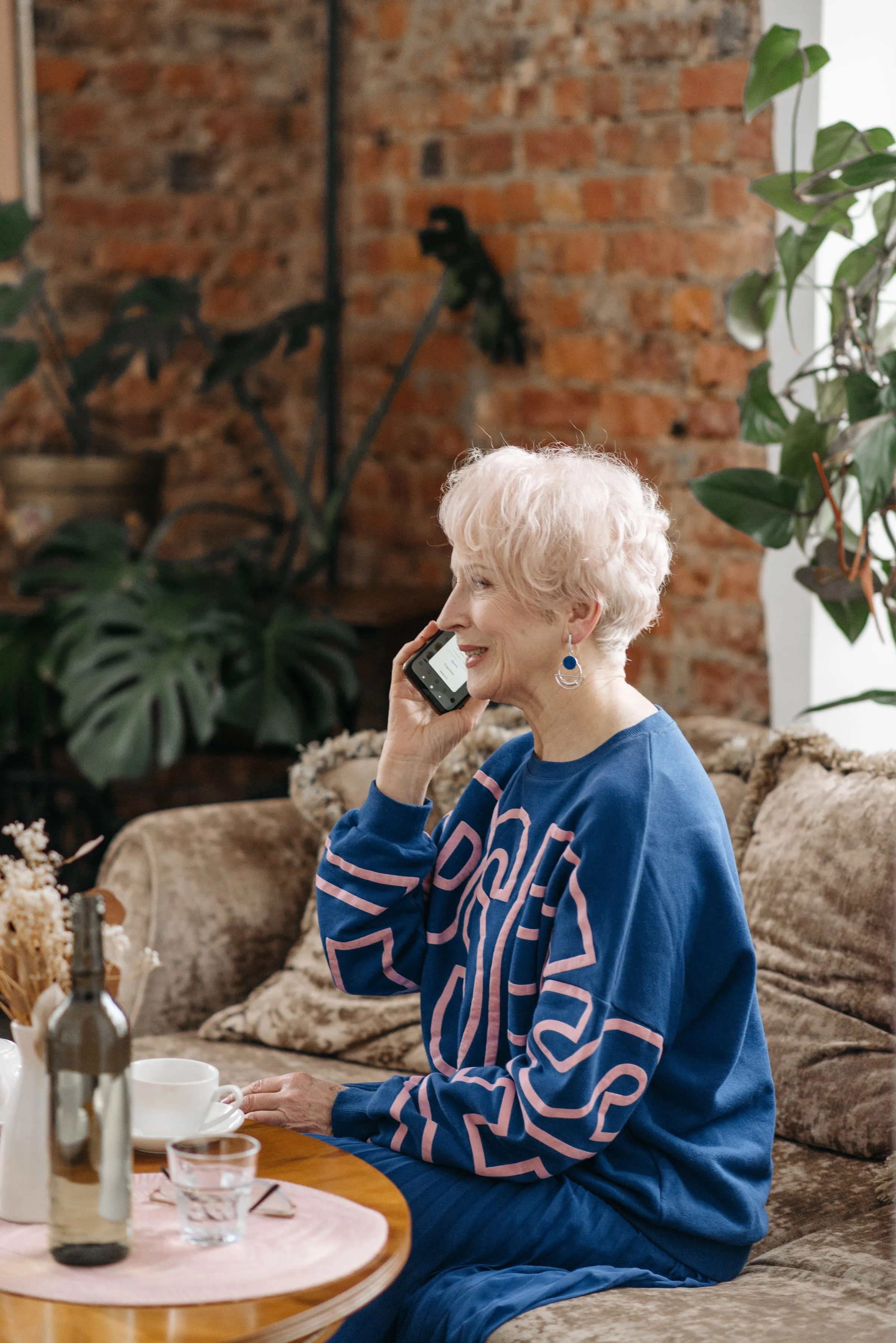 A smiling older woman talks on the phone from her living room sofa