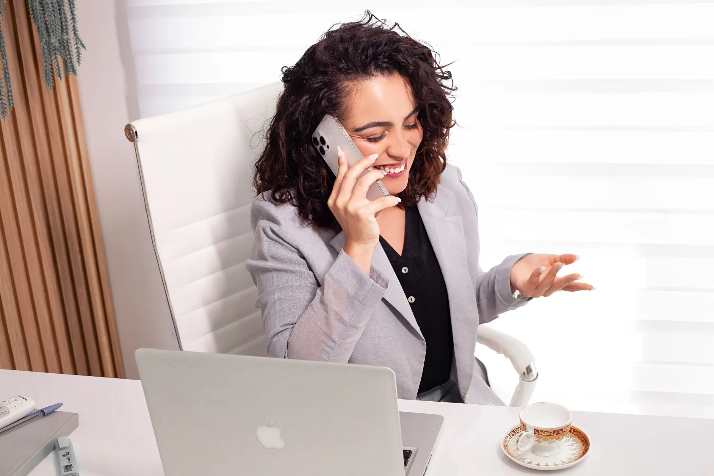 A smiling professional on a phone call at her desk, a laptop open in front of her